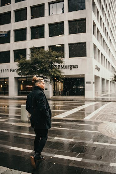 A stylish man crossing a wet street in Houston, Texas, featuring a modern office building.