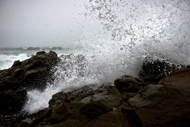 Captivating scene of ocean waves crashing against rocky shoreline under a cloudy sky.