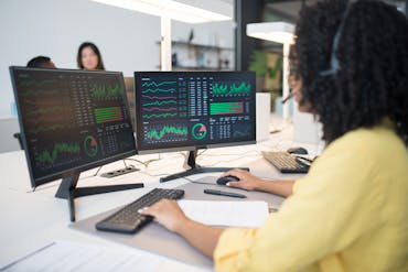 Woman analyzing financial data on dual screens at an office desk.