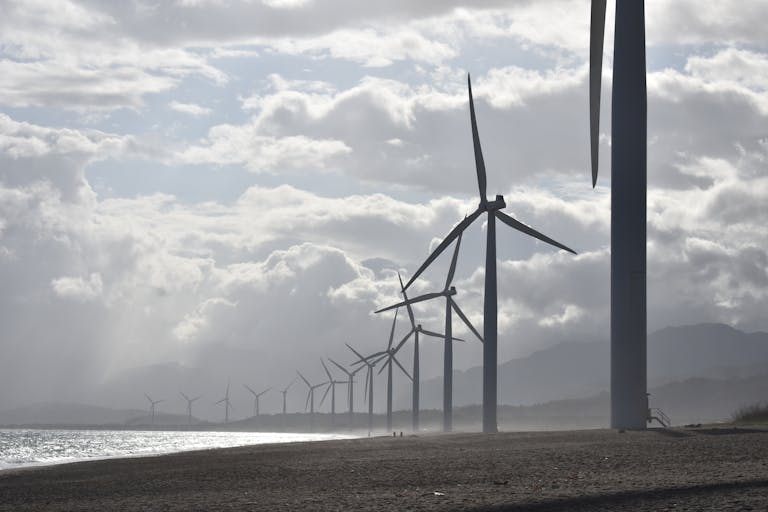 A row of wind turbines along a cloudy beach shoreline in Vigan City, Philippines.